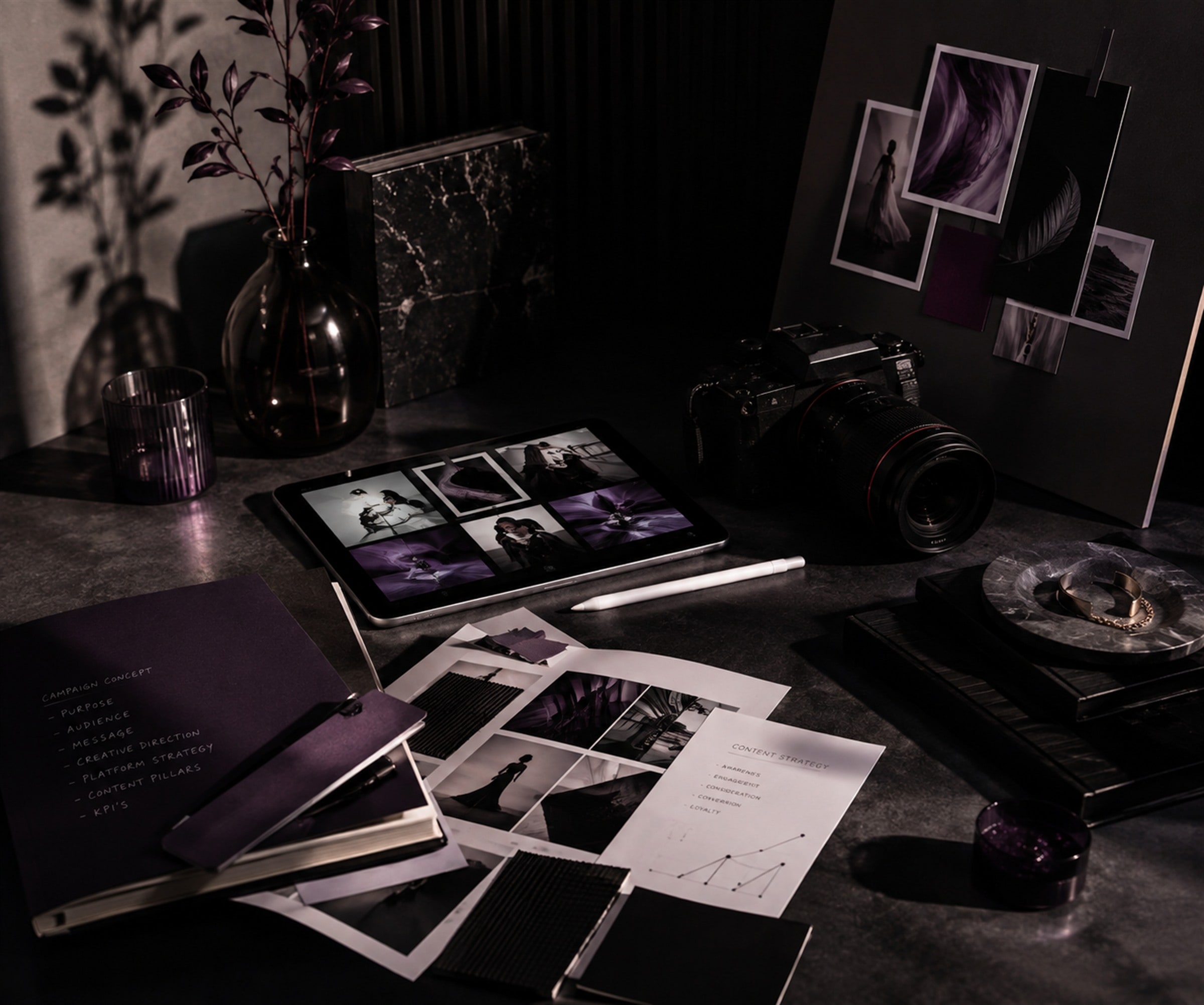 A creative studio desk layered with printed campaign photographs, contact sheets and a camera